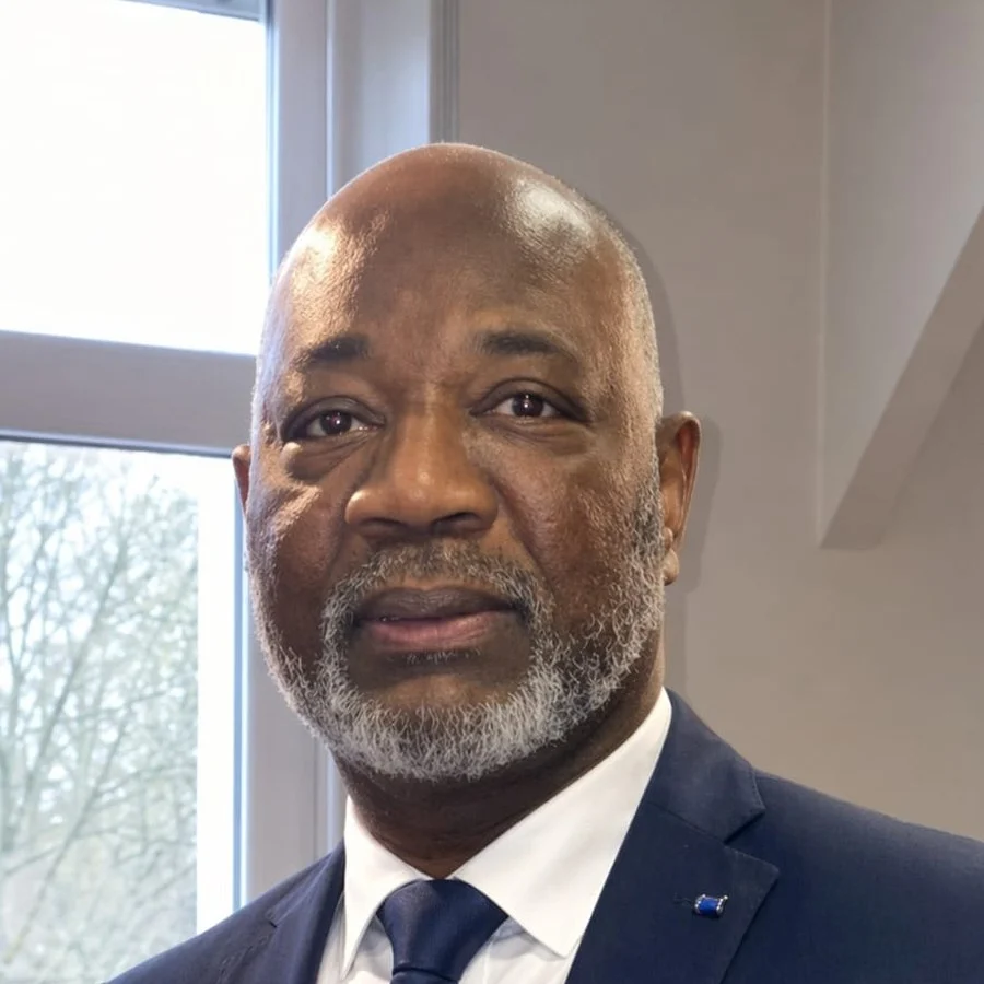 Portrait d’Amadou Diop, président de DEFI 2000, en costume sombre devant une fenêtre